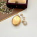 Gold locket with leaf design and a pearl and moonstone charm on a white surface.