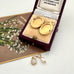 Gold locket with leaf design in a jewellery box and a pearl and moonstone charm on a white surface