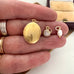 Gold locket and charms held between fingers with a jewelry box in the background.