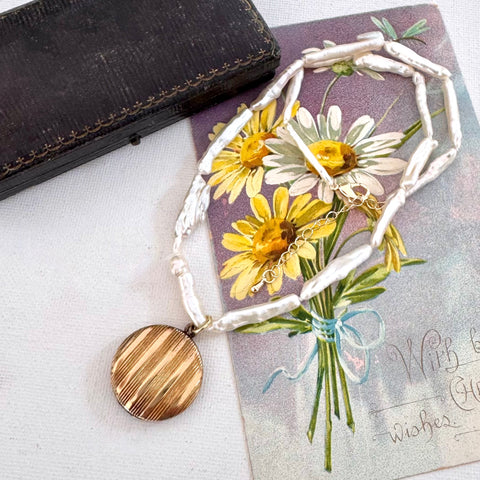 Vintage gold locket and pearl necklace on a vintage postcard of daisys.