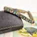 Avintage micro mosaic bracelet with a silver-toned metal frame decorated with colorful enamel medallions, resting on a dark vintage book next to a floral fan.
