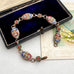 An ornate vintage-style bracelet with oval enamel medallions in red, blue, and yellow, displayed on a dark velvet jewelry box over a cream-colored card.