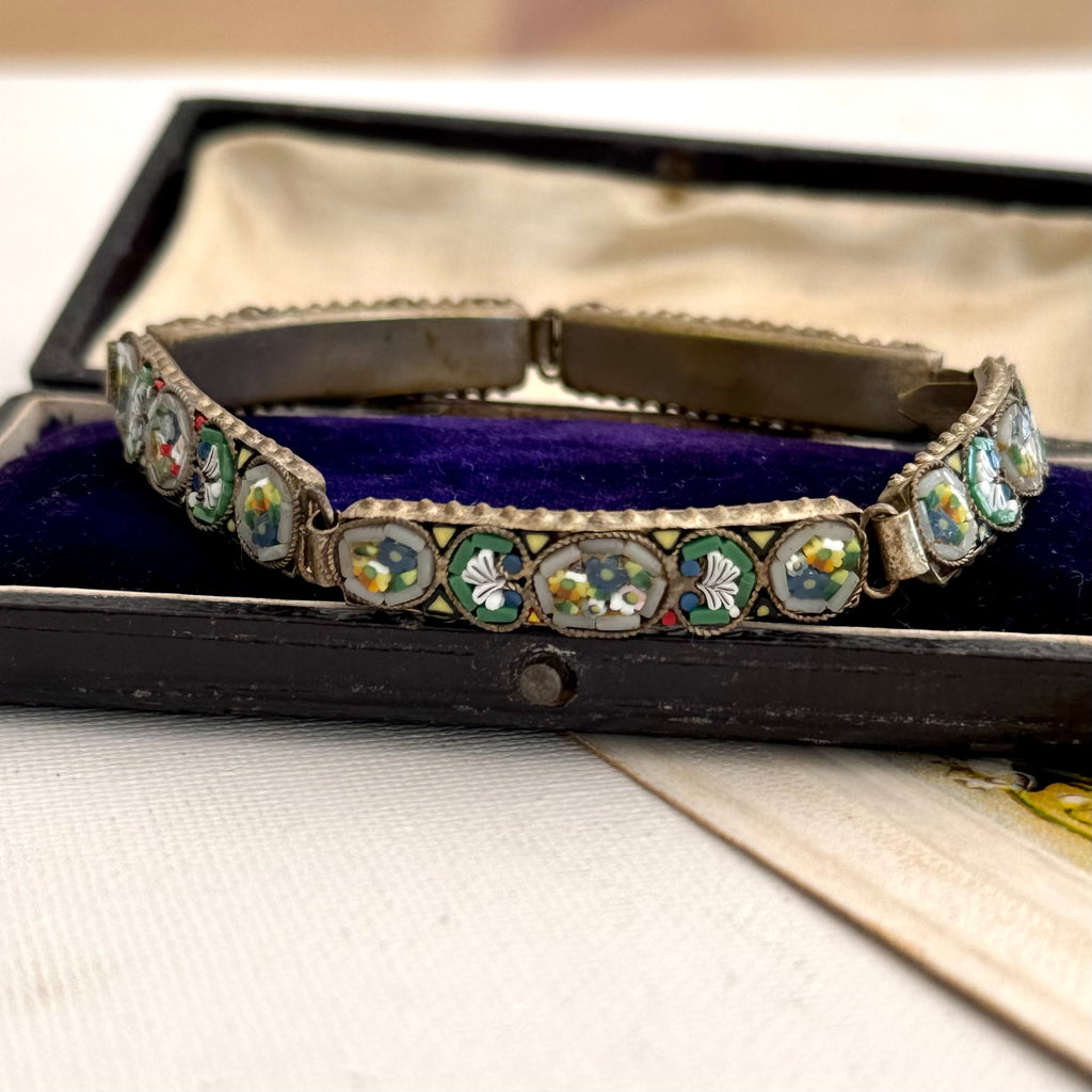 A vintage micro mosaic bracelet with green and white floral enamel inlays, displayed inside an open vintage presentation box with a purple velvet lining.
