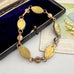 A vintage-style bracelet with oval gold-toned links and rose gold-toned chain sections, displayed on a dark velvet jewelry box next to a floral card.