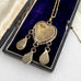 The back of a vintage micro moasic pendant and three dangling teardrop charms, displayed inside an open black velvet jewelry box.
