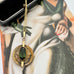A vintage Andrea Daub gold pendant necklace featuring a large oval dark green gemstone surrounded by textured gold beads and a circular gold frame, resting on a vintage illustrated card.