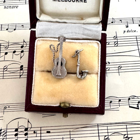 Silver guitar and saxophone charms in a jewelry box on sheet music