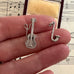 Silver guitar and saxophone charms held between fingers with sheet music in the background