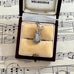 Silver guitar-shaped charm in a jewelry box on sheet music