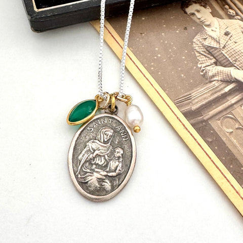 Necklace with a vintage Saint Anne pendant on a white surface next to an old photograph.
