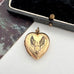 Gold heart-shaped locket with floral design on a white surface