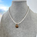 Vintage rolled gold locket and pearl necklace on a grey jewellery bust