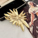Back of signed Sarah Coventry brooch from 1965 Tropics Collection on a textured surface with an open jewelry box and vintage illustration.