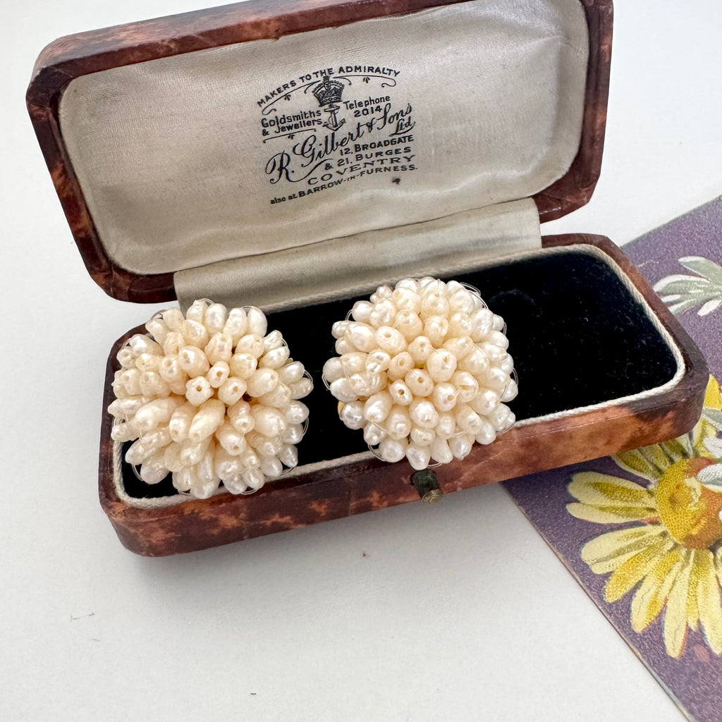 A pair of vintage signed Grosse cluster earrings made of cream-colored pearls, presented in an open antique wooden jewelry box with a black velvet lining.