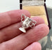 Silver tFA Cup rophy-shaped charm held between fingers with a jewelry box in the background