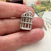 Silver birdcage charm held between fingers with a decorative background
