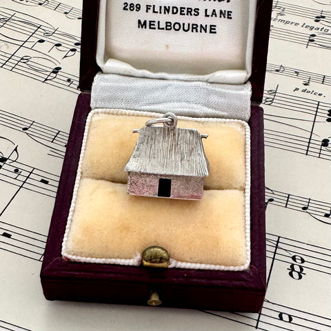 Vintage silver Fijian bure house-shaped pendant in a jewelry box on sheet music
