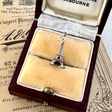 Silver Eiffel Tower charm in an open jewelry box with vintage newspaper background