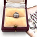 Silver bell charm in a jewelry box with a decorative card in the background