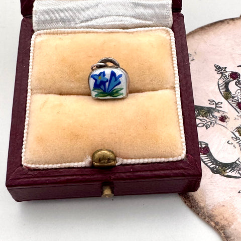 Enamel blue flower charm in a jewelry box on a white surface