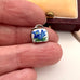 Small silver and enamel cowbell charm with floral design held between fingers