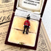 Vintage silver and enamel British Royal Foot Guard charm on display in an open jewelry box with vintage paper in the background.
