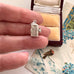 Vintage silver fridge charm held in a woman's fingers with a jewelry box with vintage card in the background