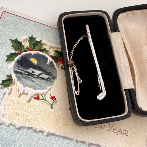 Vintage silver golf club brooch in an open jewelry box with a decorative card in the background