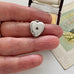 Heart-shaped silver locket held between fingers with a vintage card in the background