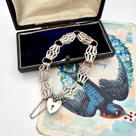 Silver bracelet with heart lock charm on an vintage card with bird illustration