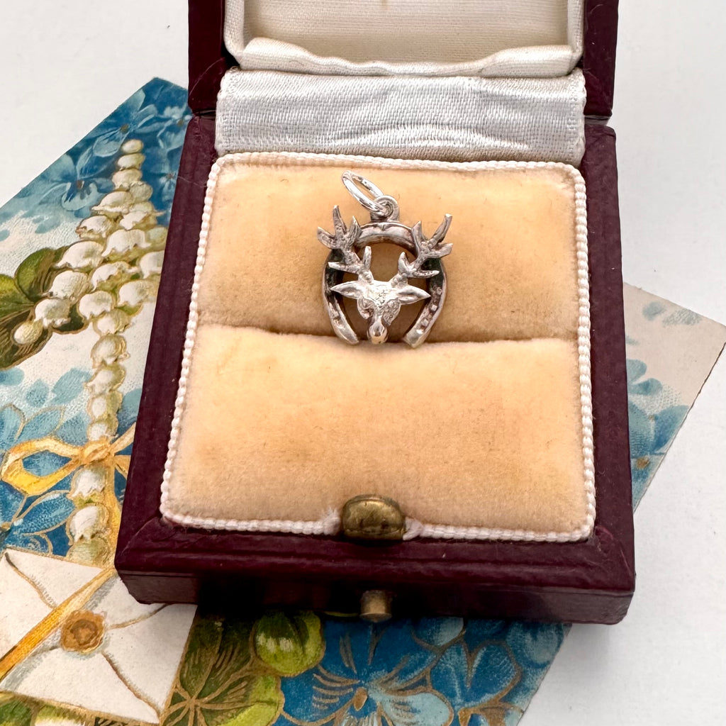 Silver deer and horseshoe charm in a jewelry box on a decorative fabric background