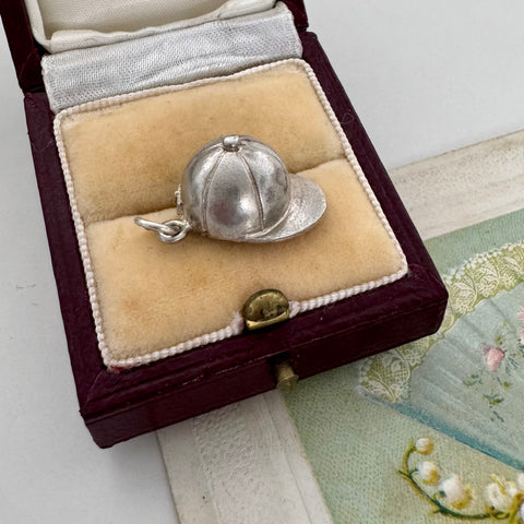 Vintage silver jockey cap charm/pendant in a jewelry box on a textured surface