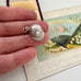 Vintage silver jockey cap charm/pendant in a woman's hands with a vintage postcard in the background