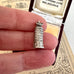 Silver Leaning Tower of Pisa charm held between fingers with vintage box in the background
