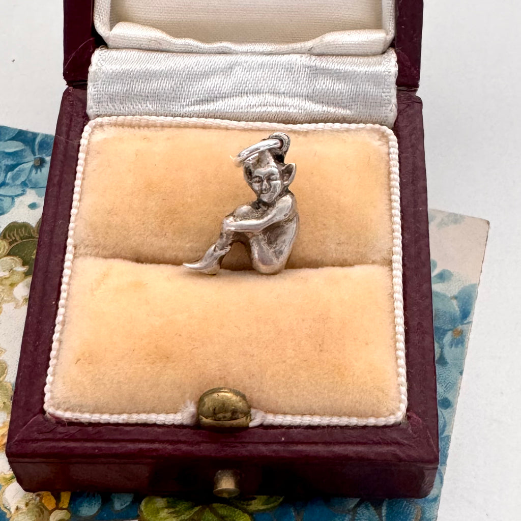 Silver pixie charm in a jewelry box with a floral patterned surface.