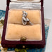 Silver pixie charm on a beige cushion in a jewelry box with a floral patterned surface.
