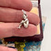 Silver pixie charm held between fingers with a floral-patterned fabric background