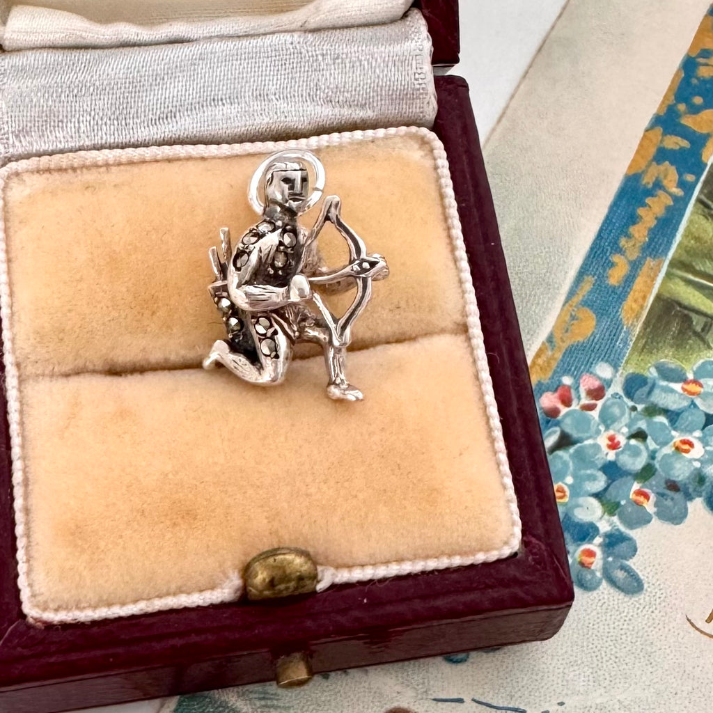 Vintage silver and marcasite archer charm in a jewelry box with a floral patterned fabric background