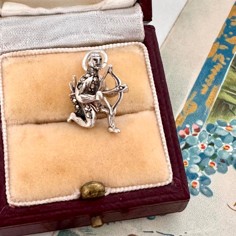 Vintage silver and marcasite archer charm in a jewelry box with a floral patterned fabric background