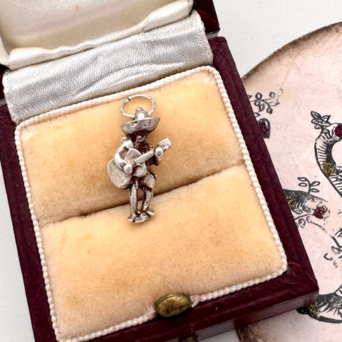 Vintage silver Mexican guitar player charm in a jewelry box with a decorative background