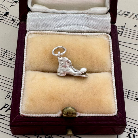 Silver vintage old boot charm in a jewellery box on sheet music background
