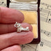 Silver old boot charm on a finger with an open jewelry box and sheet music in the background