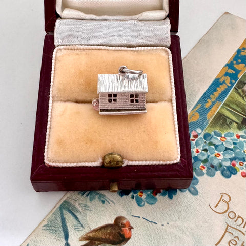 Silver house charm in a jewelry box on a decorative surface with a bird figurine.
