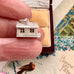 Silver house charm held between fingers with a decorative background
