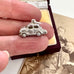 Silver car charm held between fingers with vintage photo in background