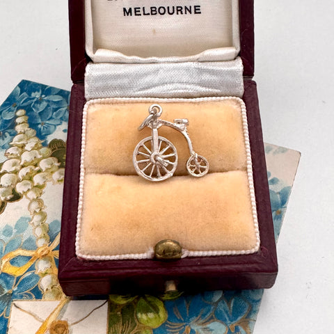 Silver bicycle charm in a jewelry box with 'Melbourne' branding on a decorative background.