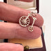 Silver bicycle-shaped charm held between fingers with a jewelry box in the background