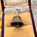 An ornate vintage silver bell-shaped charm with intricate filigree cutouts, displayed inside an open vintage burgundy jewelry box with a beige velvet lining.