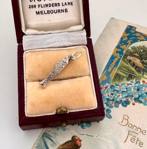 Silver fish charm in a jewelry box with vintage card in the background