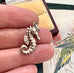 Silver seahorse charm held between fingers with a patterned background